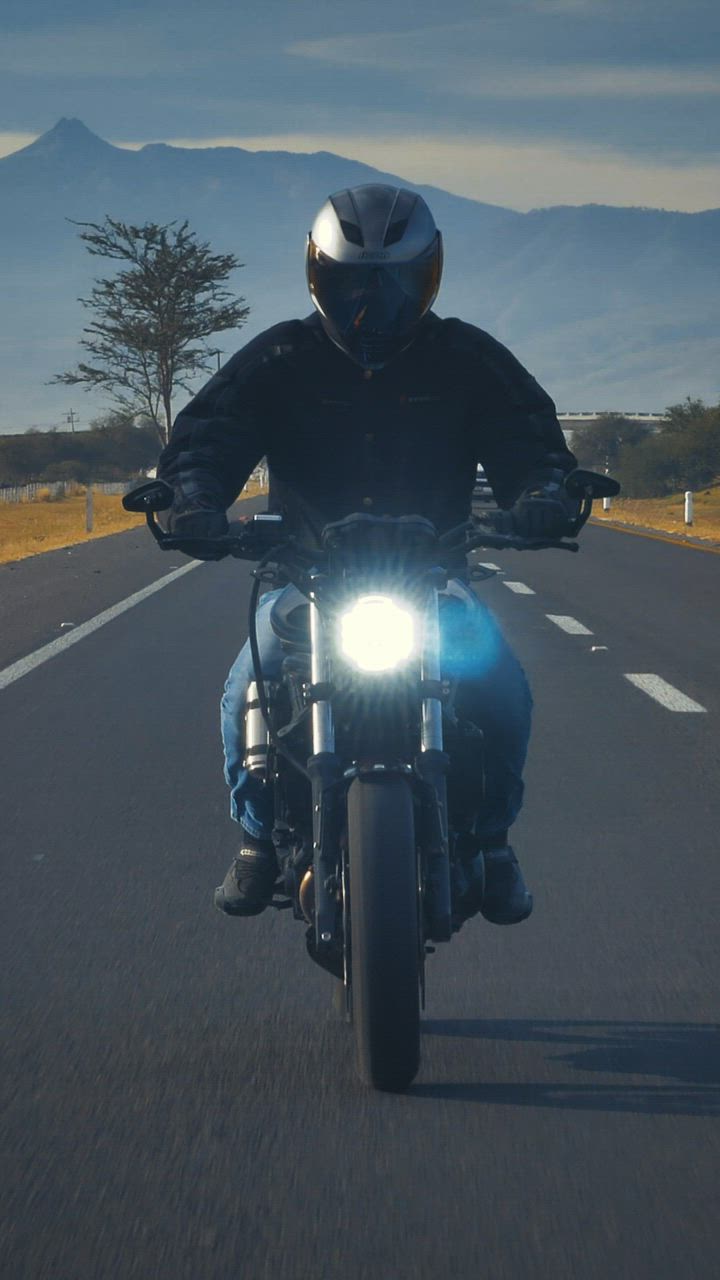 Motorradfahrer frontal auf offener Landstraße vor Bergkulisse im Morgenlicht